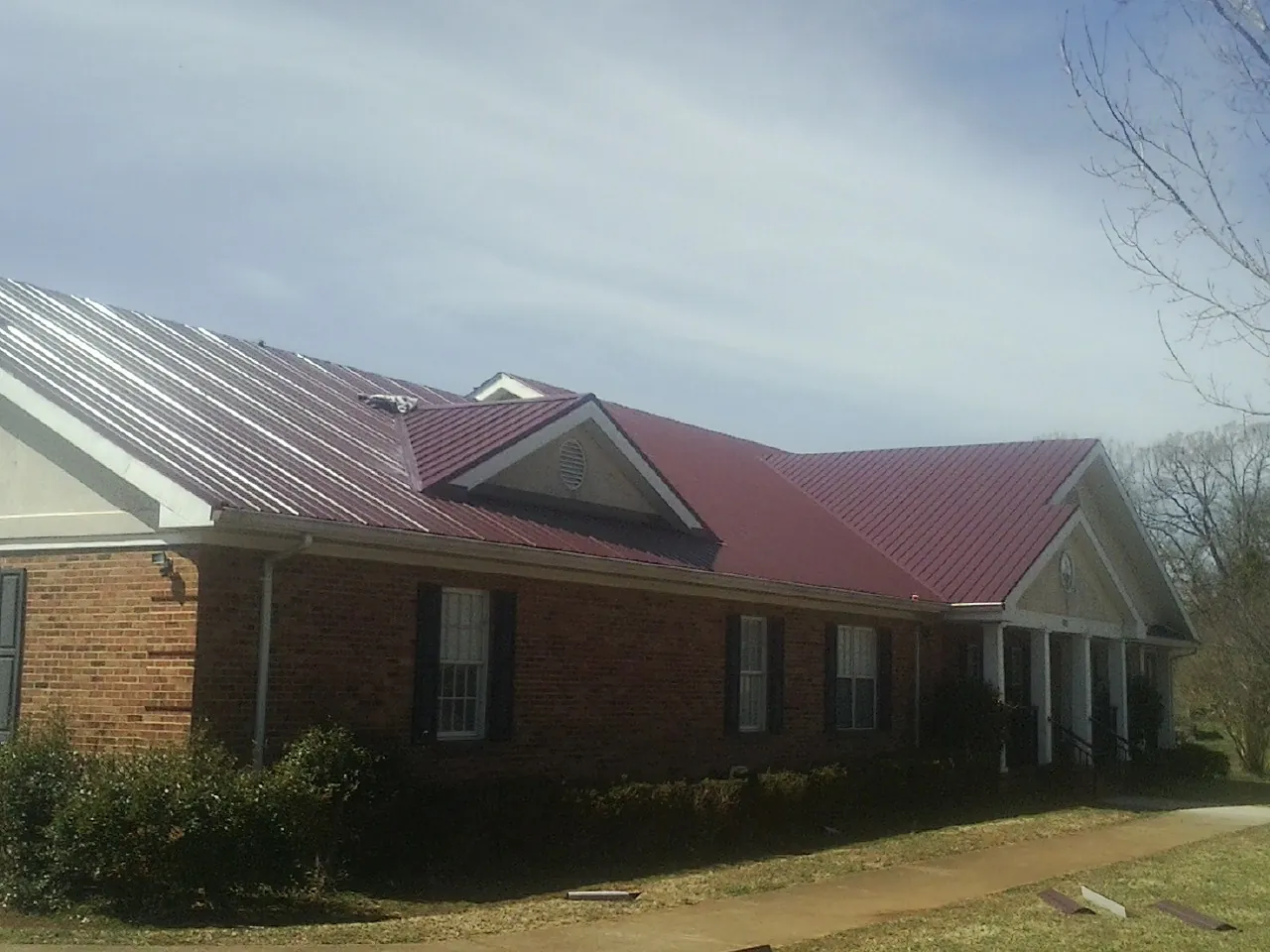 Red metal roof with gabled entries on a long brick building, from a Hail Damage Roof Repair job in Kelso