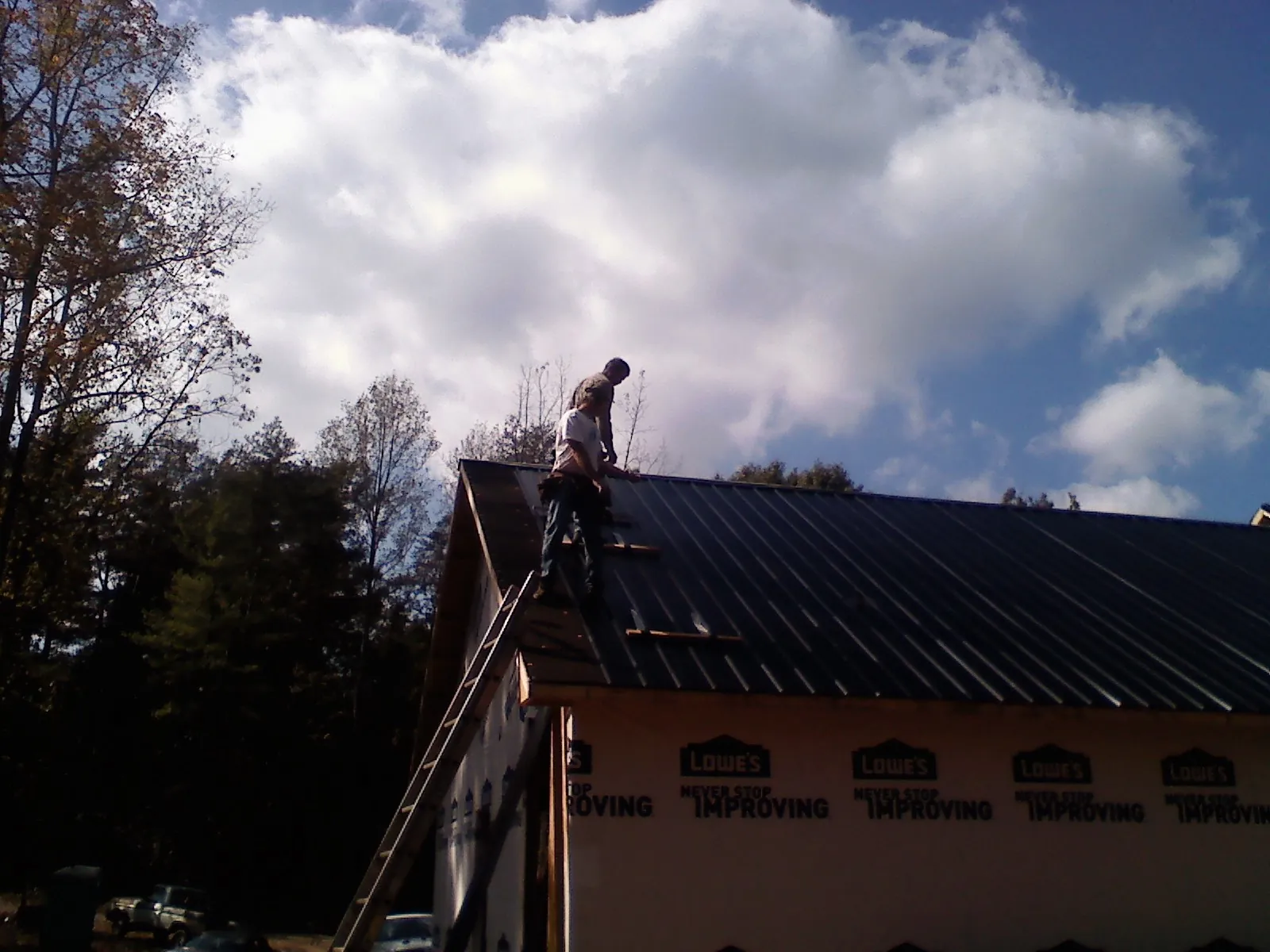 Roofer fastening dark metal panels high against a cloudy sky, from a Roof Inspection job in Kelso